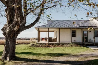 a small house with a porch and a tree at Fox Lane - Prince Edward County Farmhouse in Picton