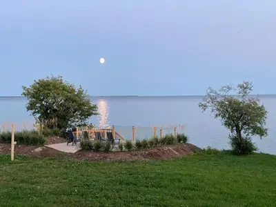 a person sitting on a bench by the water at The Hull House - Lake Ontario Waterfront w Sauna in Wellington
