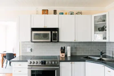 a kitchen with white cabinets and a sink and a microwave at Watson House - Century Home near Sandbanks in Cherry Valley