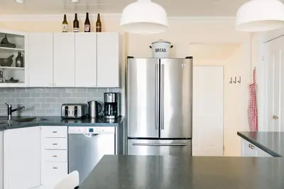 a kitchen with a stainless steel refrigerator and white cabinets at Watson House - Century Home near Sandbanks in Cherry Valley
