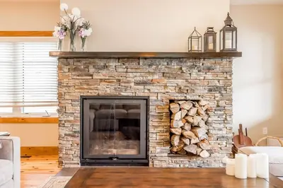 a living room with a stone fireplace with logs at Muskoka Lakeshore Cottage Bliss in Gravenhurst