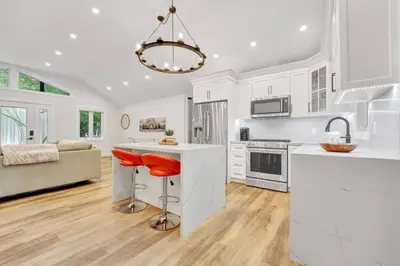 a kitchen with white cabinets and a bar with a red stool at Blue Water Dunes Cottage in Tiny