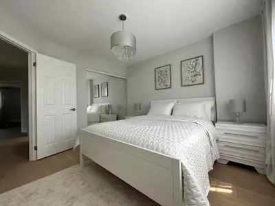 a white bedroom with a large bed and a chandelier at Lavish 4BR House Near Simcoe Lake & FH Resort in Innisfil