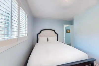 a bedroom with a bed with white sheets and windows at The Gardenhouse Cottage One in Wasaga Beach