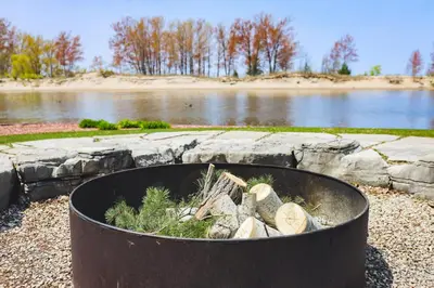 a fire pit with logs in it next to a lake at The Gardenhouse Cottage One in Wasaga Beach