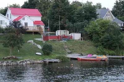 a house and a boat on a body of water at Balsam Lake Cottage 5 Bed room in Kawartha Lakes