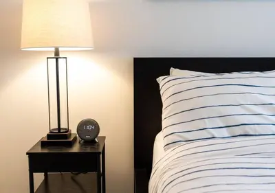 a bed with a nightstand with a clock and a lamp at Welcoming Downtown Condo with WFH setup Balcony in Toronto