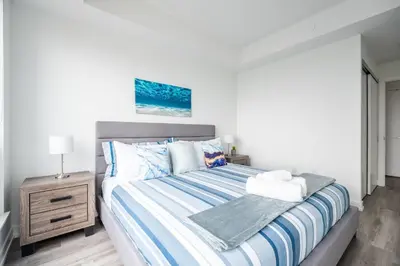 a white bedroom with a bed with blue and white sheets at 1BR Modern Condo - King Bed and Stunning City View in Kitchener