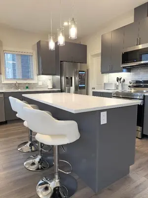 a kitchen with a large island with white bar stools at Stylish House W a Media Room Near Downtown Picton in Picton