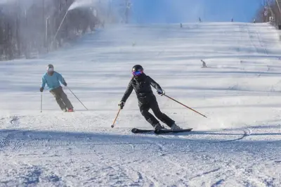 two people are skiing down a snow covered slope at Luxury 2 Level Mountain Walk Condo Sauna Jacuzzi Walk to Village in Blue Mountains