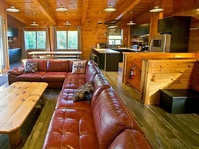 a living room with a brown leather couch and a table at Blue Mountain 6BR Chalet Modern Hot Tub Mountain Views Walk to Village in Blue Mountains