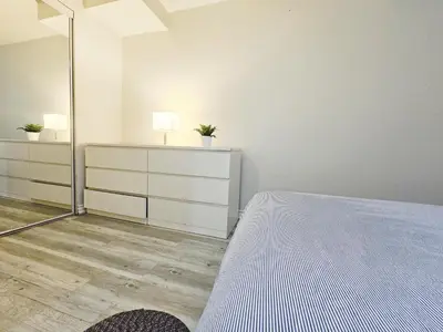 a white bedroom with a bed and a mirror at Friendly Neighborhood Garden Ave Suite in Brantford