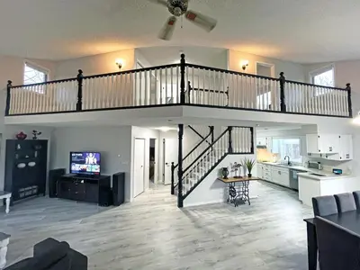 a living room with a staircase and a kitchen at Forest Retreat - Pool - Games - Fireside Joy in Cayuga