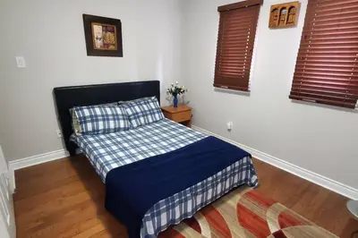 a bedroom with a bed with a blue comforter and two windows at Beautiful House in Mississauga in Mississauga