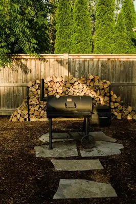 a grill with a pile of logs next to a fence at The Little White Haus in Niagara on the Lake