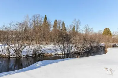 a snow covered field with trees and a river at Farm House in Coldwater