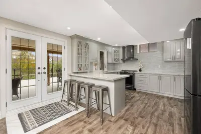 a kitchen with white cabinets and a island with bar stools at Walk-out Basement Apartment with Private Entrance in Brampton