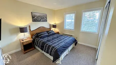 a bedroom with a bed with a blue comforter and two windows at Mountainview Loft at North Creek Resort in Blue Mountains