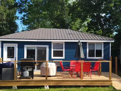 a blue house with chairs and a table on a deck at Stoneburg Cove Cottages in Carrying Place