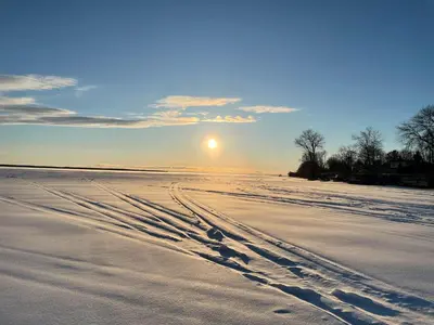 a beach with footprints in the snow with the sun in the background at Swing Bridge Cottage on Lake Simcoe - Waterfront in Brechin