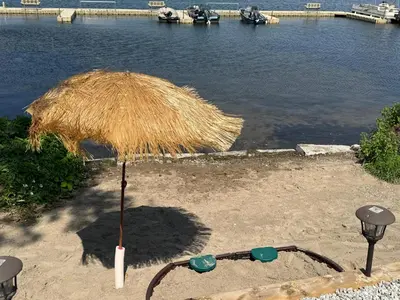 a straw umbrella sitting on the sand near the water at Sandy Shore Cottages Luxury Resort on Rice Lake in Harwood