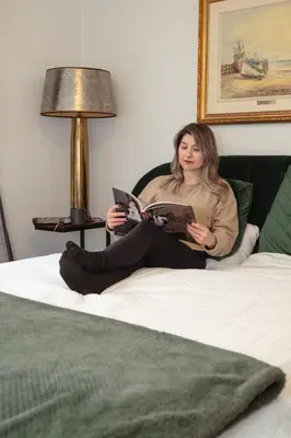 a woman sitting on a bed reading a book at Cellar House NOTL - Entire Home in the Heart of Niagara-on-the-Lake in Niagara on the Lake