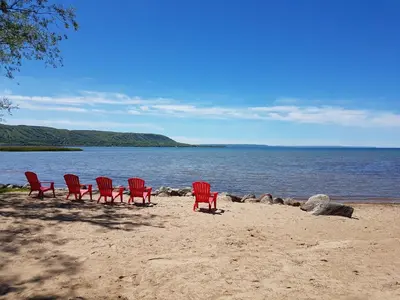 four red chairs sitting on a beach next to the water at 4 Bedroom Cottage near The Village, Private Beach Access, BBQ, Petfriendly in Blue Mountains