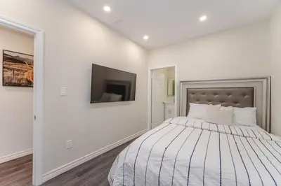 a white bedroom with a bed and a flat screen tv at Cozy basement suites Oakville in Oakville