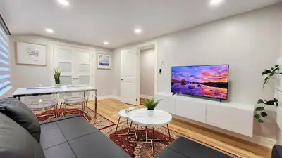 a living room with a couch and a tv on a wall at The Serene Haven Modern 2 Queen Bed Full Apartment in St. Catharines