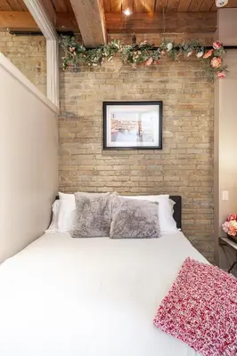 a bedroom with a white bed and a brick wall at Glyn Rhosyn Loft in Stratford