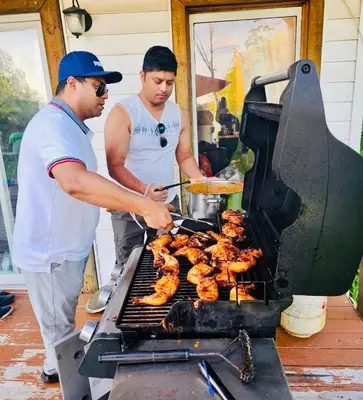 two men are cooking food on a grill at Charming Winter Cottage Retreat with Scenic Snow Views in Colborne