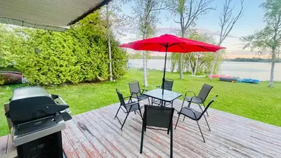 a table and chairs with a red umbrella and a grill at Charming Winter Cottage Retreat with Scenic Snow Views in Colborne