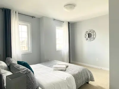 a bedroom with a bed and a chair and two windows at Stylish 3 Bdrm house- king bed, Netflix, parking in Kitchener