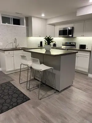 a kitchen with white cabinets and a island with stools at Brand new apartment with private entrance and patio in Guelph