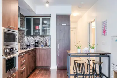 a kitchen with wooden cabinets and a bar with stools at RivetStays - The York in Toronto