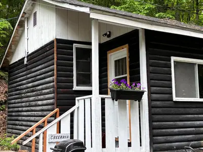 a small house with a window and flowers in a window box at Lakefront Hideaway Resort 10 Total cabins-Lake View, Private Beach in Kawartha Lakes