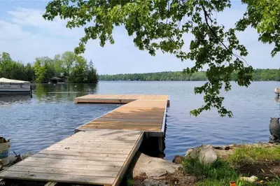a wooden dock on a lake with a boat at Waterfront Cottage - Fireplace - Kawartha in Lakefield