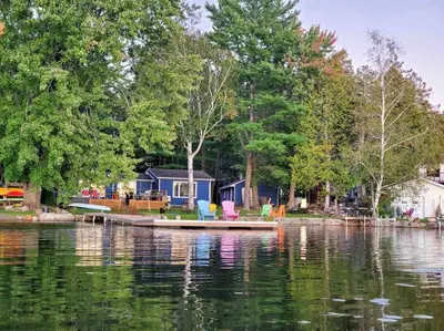 a small boat on a lake with a house at Waterfront Cottage - Fireplace - Kawartha in Lakefield