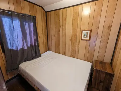 a small bed in a wooden room with a window at Tiny Wood Cottage 14 in Wasaga Beach