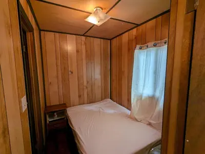 a small bed in a wooden room with a window at Tiny Wood Cottage 23 in Wasaga Beach