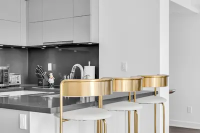a kitchen with white cabinets and gold stools at The Royal 2 Bedroom Condo Yorkville in Toronto