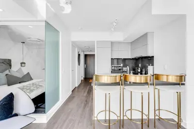 a bedroom with a bed and a kitchen with gold bar stools at The Royal 2 Bedroom Condo Yorkville in Toronto