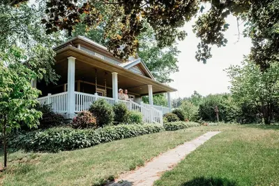 a woman standing on the porch of a house at Vintage Farmhouse with Hot Tub on Vineyard in Waterford