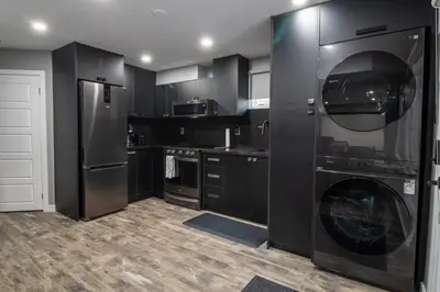a kitchen with black cabinets and a washing machine at The Gate Chic & Cozy Basement Retreat in Ajax in Ajax