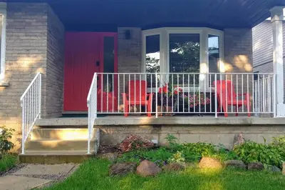 a house with a red door and red chairs on the porch at Birdsong Bungalow in Port Dover