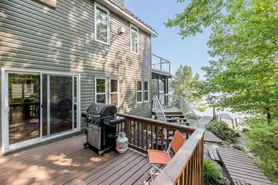 a deck with a grill and chairs on a house at Muskoka Lakeshore Cottage Bliss in Gravenhurst