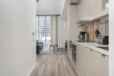 a kitchen with white cabinets and a living room at 1BD next to Queen St - most ideal location in Toronto