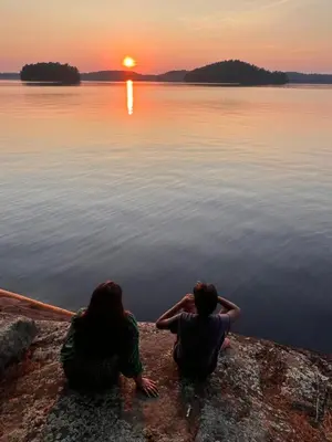 two people sitting on the edge of a lake watching the sunset at Birkswyld waterfront cottage Mary Lake in Huntsville