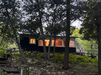 a black house in the middle of some trees at Birkswyld waterfront cottage Mary Lake in Huntsville