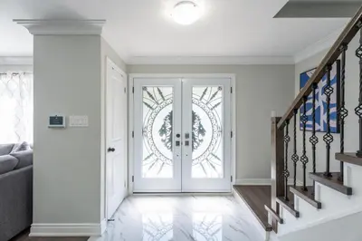 a white hallway with a glass door and stairs at Chic and Cozy 5 Bedroom House in Brampton